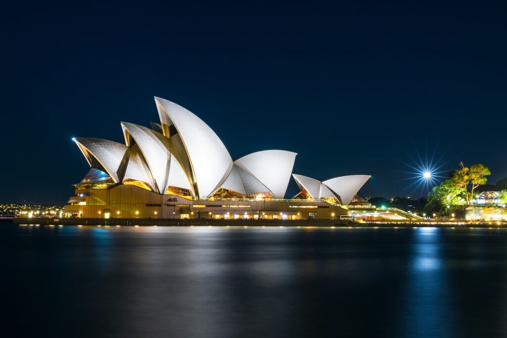 Operahuset i Sydney om natten, oplyst nedefra, hvilket fremhæver bygningens ikoniske sejlformede tage mod en mørk nattehimmel.