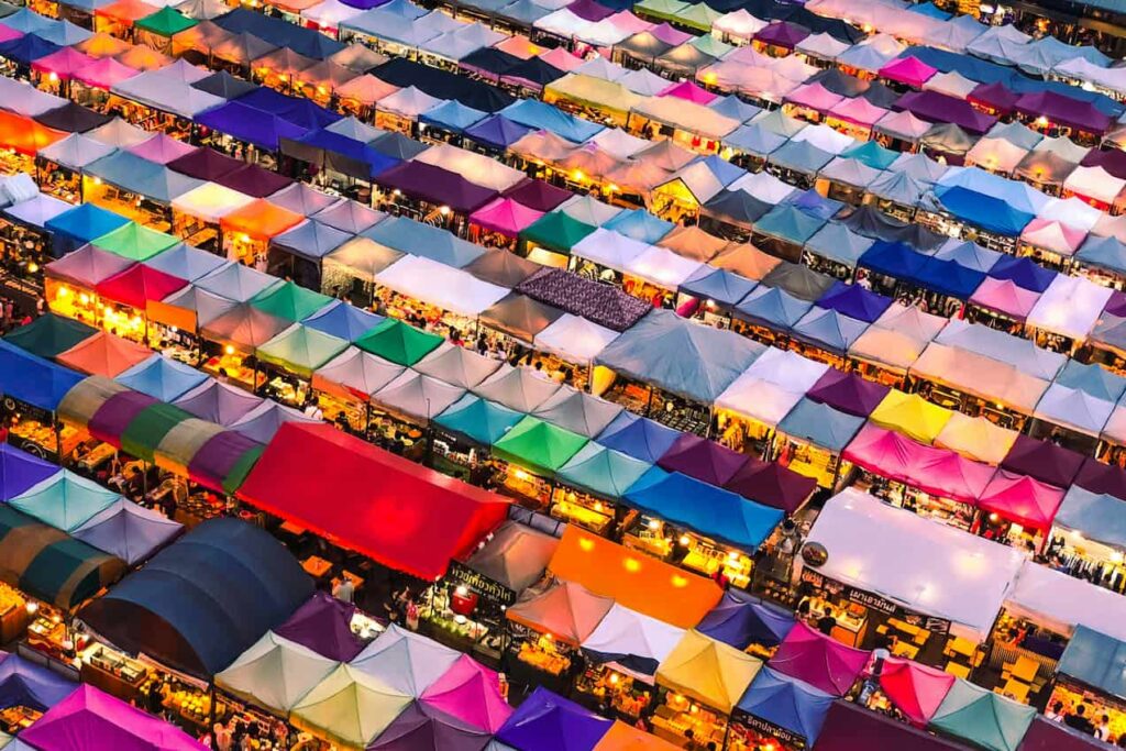 Bangkok's Train Night Market set ovenfra, hvor de farverige telte og boder strækker sig i alle retninger. Markedet summer af aktivitet med levende farver og et væld af boder, der tilbyder alt fra mad til souvenirs.