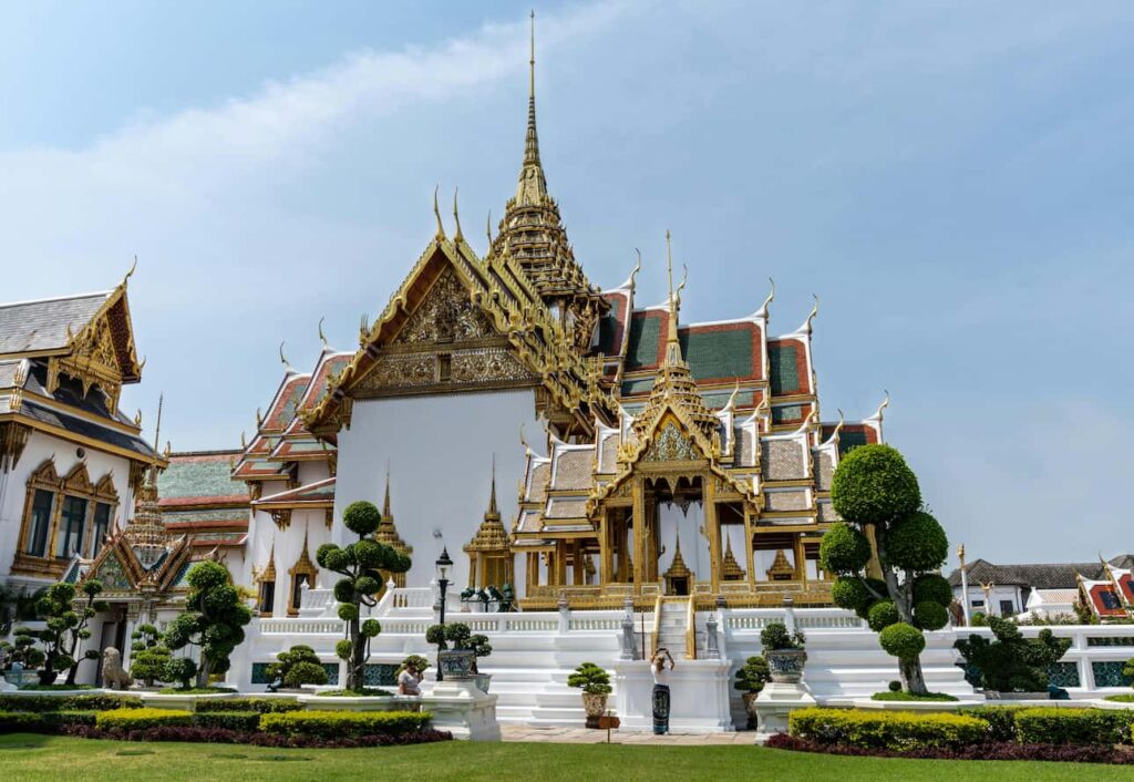 Wat Phra Kaew tempel, beliggende i Bangkok, Thailand, prydet med forgyldte spir og detaljerede thailandske arkitektoniske elementer, omgivet af frodige grønne haver og en rolig atmosfære.