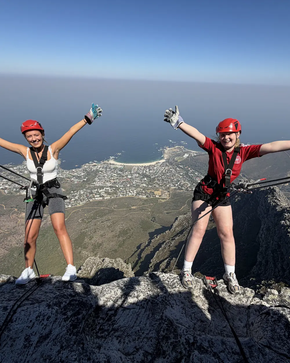 To rejsende med armene i vejret på kanten af et bjerg over Cape Town