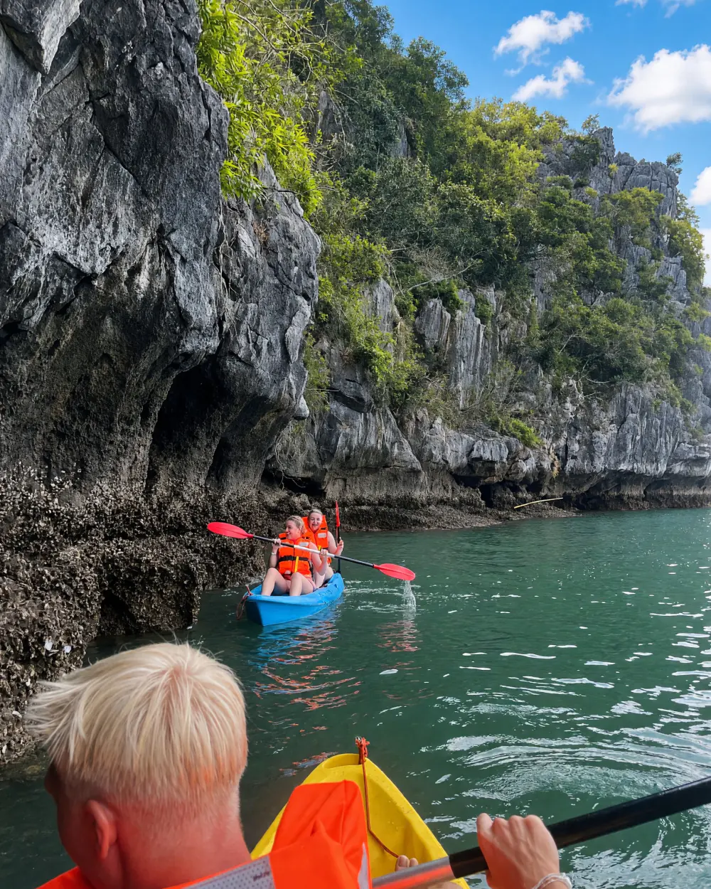 Rejsende padler i kajak mellem kalkstensklipperne i Ha Long Bay